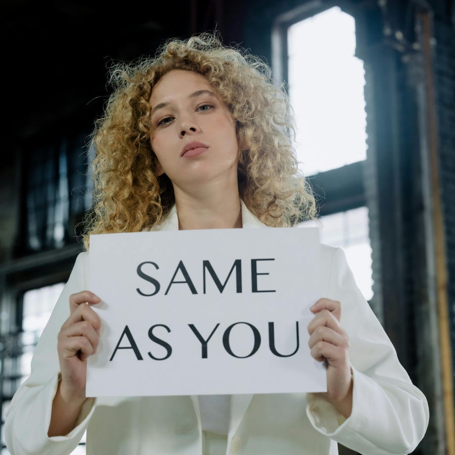 Woman with curly hair holding a 'Same as You' sign, promoting equality indoors.