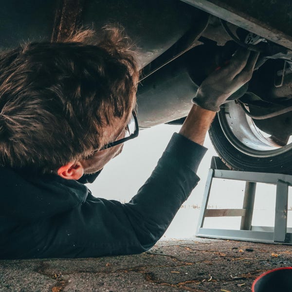 Mechanic skillfully repairing car undercarriage in outdoor setting with tools.