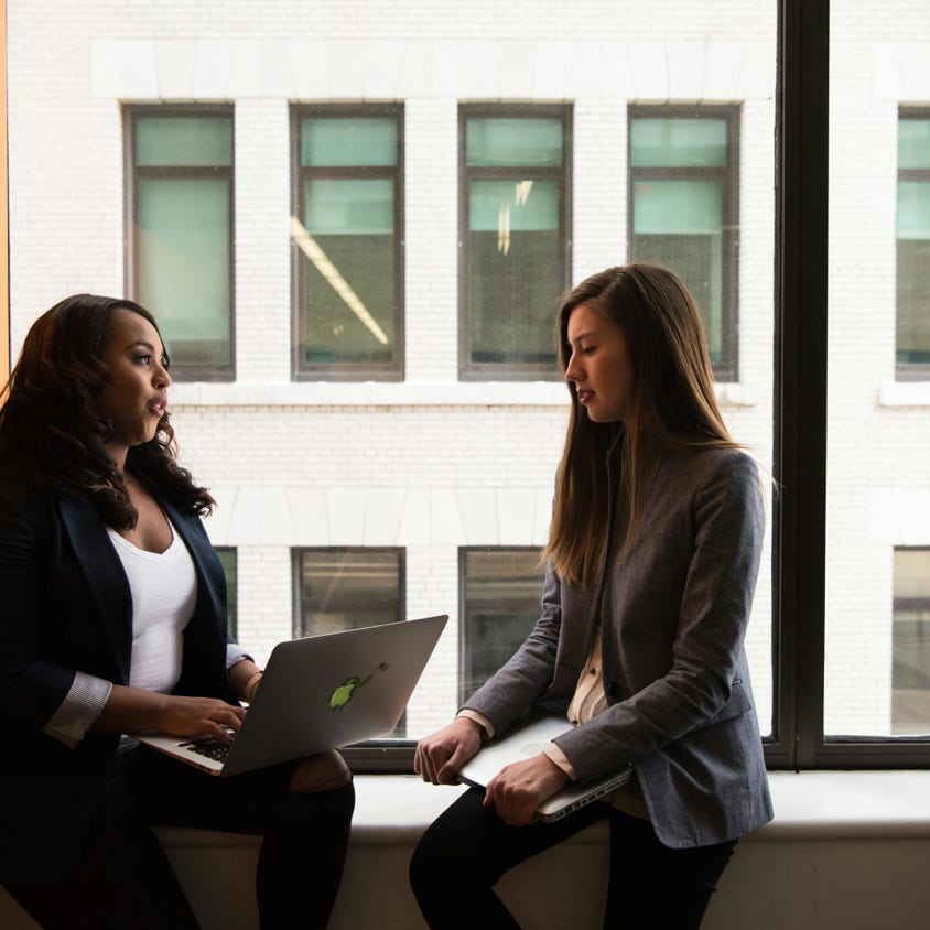 Two women having a business discussion in an office setting, using a laptop.